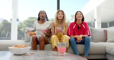 Heyecanlı çeşitli bayan arkadaşlar, ellerinde cipsler ve içkilerle TV 'de spor izliyorlar, ağır çekimde. Spor, eğlence, boş zaman, arkadaşlık ve yaşam tarzı.