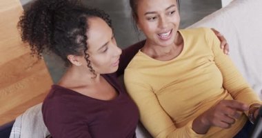 Çift ırklı mutlu lezbiyen çift koltukta birlikte dinleniyor, tablet kullanıyor ve kucaklaşıyorlar, ağır çekimde. Yaşam tarzı, ilişki, birliktelik, rahatlama, aşk ve ev hayatı, değişmemiş..
