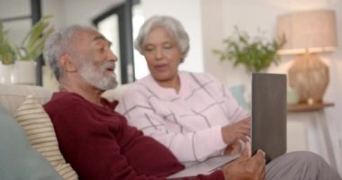 Kanepede oturan ve dizüstü bilgisayar kullanan, değiştirilmemiş, ağır çekimde mutlu çift. Kıdemli yaşam tarzı, iletişim ve ev hayatı.