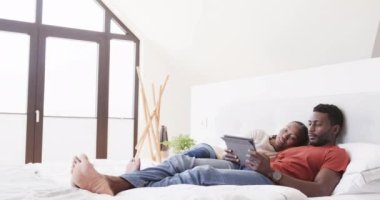 Afro-Amerikalı mutlu çift yatakta tablet kullanıyor, ağır çekimde. Yaşam tarzı, ilişki, rahatlama, iletişim, birliktelik, aşk ve aile hayatı, değişmemiş..