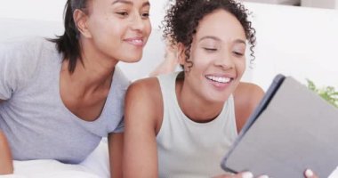 Çift ırklı mutlu çift yatakta tablet kullanarak ağır çekimde yatıyor. Yaşam tarzı, ilişki, birliktelik, rahatlama, iletişim ve ev hayatı, değişmemiş..