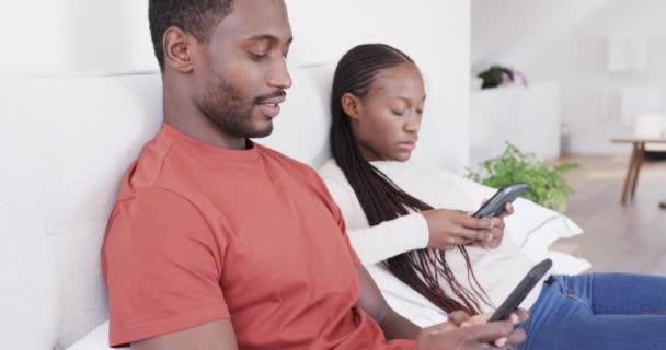 アフリカ系アメリカ人のカップルは 両方のスマートフォンを使用して ゆっくりとした動きでベッドに座っている リラックス コミュニケーションと国内生活 変更なし — ストック動画