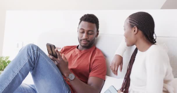 幸せなアフリカ系アメリカ人のカップルのベッドで話をし スマートフォンを使用して座って スローモーションで リラクゼーション コミュニケーション 一緒に 愛と国内生活 変わらない — ストック動画