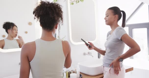 快乐的一对女同性恋夫妇在阳光灿烂的浴室里刷牙和使用智能手机 动作缓慢 生活方式 自我照顾 沟通和家庭生活 保持不变 — 图库视频影像