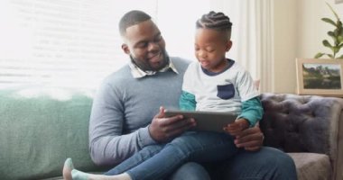 Mutlu Afro-Amerikan babası koltukta oğlunun kucağında ağır çekimde tablet kullanarak oturuyor. Aile, iletişim, birliktelik ve aile hayatı değişmedi..