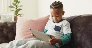Mutlu Afro-Amerikan çocuk koltukta ağır çekimde tablet kullanıyor. Yaşam tarzı, iletişim, çocukluk ve ev hayatı, değişmemiş..