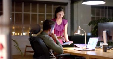 Geceleri ofiste tablet ve dizüstü bilgisayar kullanarak iş tartışan çeşitli erkek ve kadın meslektaşlar. İş, iletişim, ofis, takım çalışması, teslim tarihi ve geç saatlere kadar çalışma, değiştirilmemiş.