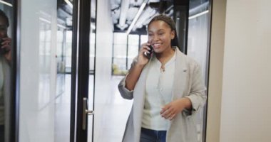 Mutlu Afro-Amerikan iş kadını ofis koridorunda telefonla konuşuyor, ağır çekimde. İş, iletişim, ofis ve iş, değiştirilmemiş.