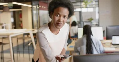 Afrika kökenli Amerikalı sıradan bir iş kadınının portresi akıllı telefonu kullanarak ofise gülüyor, ağır çekimde. İş, iletişim, güven, ofis ve iş, değiştirilmemiş.