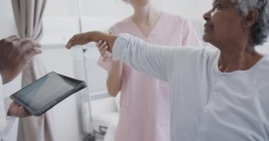 Tabletli çeşitli erkek doktor ve mutlu kadın fizyoterapisti yaşlı kadın hastayı yavaş çekimde tedavi ediyor. Sağlık hizmetleri, hastane, takım çalışması, kontrol, fizyoterapi ve sağlık hizmetleri, değiştirilmemiş.