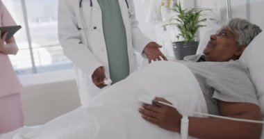 Mutlu kadın doktor, tabletli hemşire ve yatağında konuşan yaşlı hasta, ağır çekimde. Sağlık hizmetleri, takım çalışması, kontrol, kıdemli sağlık, hastane ve sağlık hizmetleri, değiştirilmemiş.