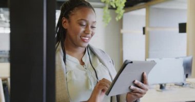 Mutlu Afro-Amerikan günlük iş kadını ofiste duran tableti kullanıyor, ağır çekimde. İş, iletişim, ofis ve iş, değiştirilmemiş.