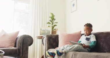 Mutlu Afro-Amerikan çocuk koltukta ağır çekimde tablet kullanıyor. Yaşam tarzı, iletişim, çocukluk ve ev hayatı, değişmemiş..