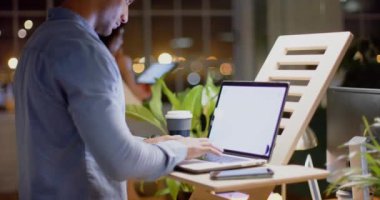 Çift ırklı iş adamı, geceleri masa başında fotokopi çekerek dizüstü bilgisayar kullanıyor. İş, iletişim, günlük ofis, teslim tarihi ve geç saatlere kadar çalışma, değiştirilmemiş.