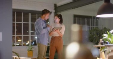 Gece ofiste konuşan ve tablet kullanan farklı erkek ve kadın meslektaşlar. İş, iletişim, günlük ofis, takım çalışması, son teslim tarihi ve geç saatlere kadar çalışma, değiştirilmemiş.
