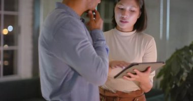 Gece ofiste konuşan ve tablet kullanan farklı erkek ve kadın meslektaşlar. İş, iletişim, günlük ofis, takım çalışması, son teslim tarihi ve geç saatlere kadar çalışma, değiştirilmemiş.
