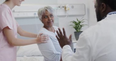 Çeşitli erkek doktor ve kadın fizyoterapi uzmanları gülümseyen yaşlı kadın hastayı yavaş çekimde tedavi ediyor. Sağlık hizmetleri, hastane, kontrol, takım çalışması, fizyoterapi ve sağlık hizmetleri, değiştirilmemiş.