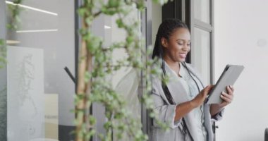 Mutlu Afro-Amerikan sıradan iş kadını ofis odasında tablet kullanıyor, ağır çekimde. İş, iletişim, ofis ve iş, değiştirilmemiş.