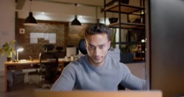Geceleri ofisteki bilgisayarları kullanarak çift ırklı iş adamına odaklanmış, ağır çekim. İş, iletişim, günlük ofis, teslim tarihi ve geç saatlere kadar çalışma, değiştirilmemiş.