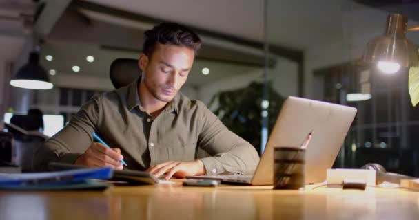 Занятой Бизнесмен Сидящий Столом Использует Ноутбук Делает Заметки Офисе Ночью — стоковое видео