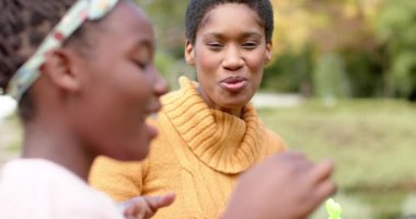 Mutlu Afro-Amerikan anne ve kızı güneşli bahçede kabarcıklar çıkarıyor. Aile, çocukluk, bahar, mutluluk, yaşam tarzı, rahatlama, değişmemiş.