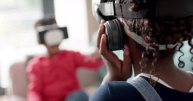 Afrika kökenli Amerikalı kız ve erkek kardeşler oturma odasında ağır çekimde VR kulaklık kullanıyor. Aile, iletişim, çocukluk, aile hayatı, değişmemiş.