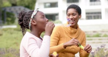 Mutlu Afro-Amerikan anne ve kızı güneşli bahçede kabarcıklar çıkarıyor. Aile, çocukluk, bahar, mutluluk, yaşam tarzı, rahatlama, değişmemiş.