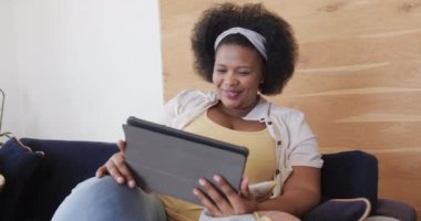 Tablet kullanan, gülümseyen, değişmeyen, ağır çekimde gülümseyen Afro-Amerikan kadın portresi. Yaşam tarzı, beden içeriği, iletişim ve ev hayatı..