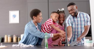 Mutlu Afro-Amerikan ebeveynler, oğlu ve kızı bulaşık yıkıyor ve mutfakta gülümsüyor, ağır çekimde. Aile, çocukluk, aile hayatı, değişmemiş..