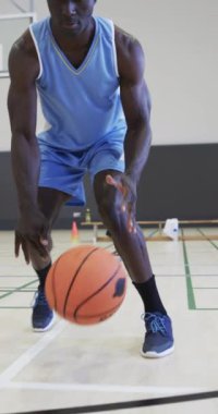 Erkek Afro-Amerikan basketbolcunun kapalı sahada ağır çekimde antrenman yaptığı dikey video. Spor, fitness, sağlık ve açık hava aktiviteleri, değiştirilmemiş.