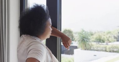 Düşünceli Afro-Amerikan artı cüsseli kadın pencereden bakıyor, değiştirilmemiş, ağır çekimde. Yaşam tarzı, beden içeriği ve ev hayatı..