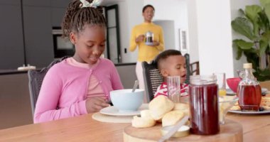 Afro-Amerikalı çocuk yemek yiyor ve kız mutfakta Smatphone kullanıyor, ağır çekimde. Aile, iletişim, çocukluk, yaşam tarzı ve aile hayatı, değişmedi..