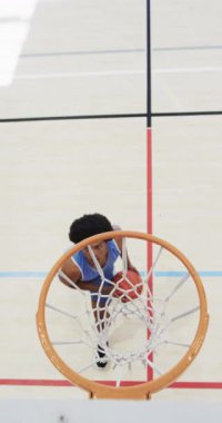 Erkek Afro-Amerikan basketbolcunun kapalı sahada ağır çekimde antrenman yaptığı dikey video. Spor, fitness, sağlık ve açık hava aktiviteleri, değiştirilmemiş.