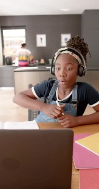 Afro-Amerikan bir kızın kulaklık takıp internetten el kaldırdığı dikey video. Ağır çekimde. Eğitim, çocukluk, iletişim, çevrimiçi öğrenme ve ev hayatı, değiştirilmemiş.