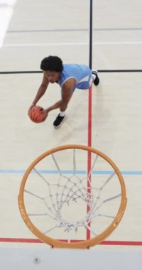 Erkek Afro-Amerikan basketbolcunun kapalı sahada ağır çekimde antrenman yaptığı dikey video. Spor, fitness, sağlık ve açık hava aktiviteleri, değiştirilmemiş.