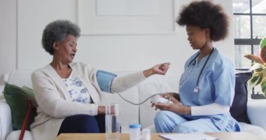 Afro-Amerikalı kadın doktor, yaşlı kadın hastanın tansiyonunu ölçüyor, ağır çekimde. Sağlık hizmetlerini, sağlık hizmetlerini ve yaşlı yaşam tarzını kontrol edin..