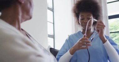 Steteskoplu mutlu Afro-Amerikan bayan doktor yaşlı bayan hastayla konuşuyor, ağır çekimde. Sağlık hizmetlerini, sağlık hizmetlerini ve yaşlı yaşam tarzını kontrol edin..