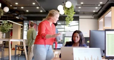 Bilgisayarları kullanan ve sıradan ofislerde konuşan mutlu bayan meslektaşlar, yavaş çekim. İş, takım çalışması, iletişim ve günlük ofis, değiştirilmemiş.