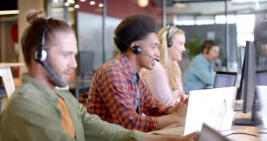 Çift ırklı mutlu iş adamı ve çeşitli meslektaşları telefon kulaklığı ve ağır çekim kullanıyor. İş, takım çalışması, teknoloji, iletişim ve gündelik ofis, değiştirilmemiş.