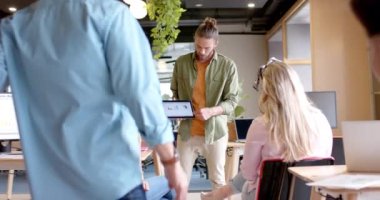 Kafkasyalı sıradan iş adamı çeşitli meslektaşlarına ofisinde tabletle sunuyor, ağır çekimde. İş, günlük ofis, takım çalışması ve sunum, değiştirilmemiş.