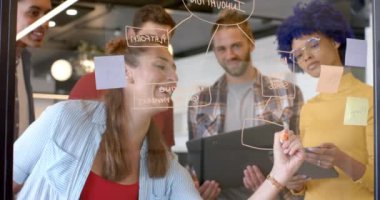 Cam duvara notlar yazarak beyin fırtınası yapan çeşitli yaratıcı meslektaşların kutlu olsun. Günlük ofis, takım çalışması, beyin fırtınası, iletişim, iş ve yaratıcı çalışma, değiştirilmemiş.