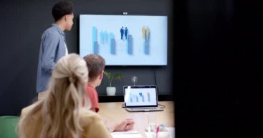 Çift ırklı iş adamı, ofis toplantısındaki çeşitli meslektaşlarına ağır çekimde mutlu bir sunum yapıyor. İş, iletişim, sunum, toplantı, günlük ofis ve iş, değiştirilmemiş.