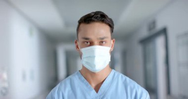 Yüz maskesi takan mutlu çift ırklı erkek doktorun portresi, yavaş çekim. Hastane, ilaç ve sağlık hizmetleri değiştirilmemiş..
