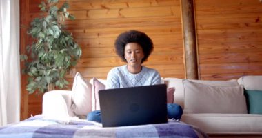 Mutlu Afrikalı Amerikalı kadın oturma odasında dizüstü bilgisayar kullanıyor, ağır çekimde. Rahatlama, iletişim, yaşam tarzı ve ev hayatı, değişmemiş..
