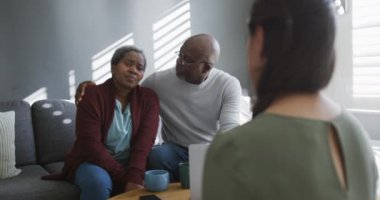 Asyalı kadın finans danışmanı evdeki kanepede oturan Afrikalı Amerikalı son sınıf öğrencisiyle konuşuyor. üst düzey sağlık, destek ve yaşam tarzı.