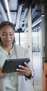 Ofiste tablet kullanan mutlu Afro-Amerikan iş kadınının dikey video portresi, yavaş çekim. İş, teknoloji ve iş.