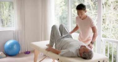 Çeşitli erkek fizyoterapist tavsiyeleri ve ağır çekimde kanepede egzersiz yapan yaşlı erkek hasta. Fizyoterapi, sağlık, refah ve yaşlı yaşam tarzı değişmedi..