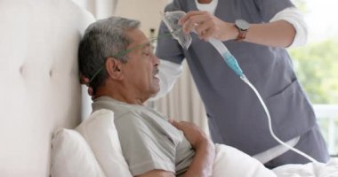 Çeşitli erkek doktorlar, yaşlı erkek hastalara evde oksijen maskesi takmalarında yardımcı oluyor, ağır çekimde. Sağlık hizmetleri, kontrol, ev ziyareti, sağlık hizmetleri, refah ve yaşlı yaşam tarzı, değişmemiş..