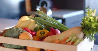 Güneşli mutfakta tezgahın üstünde bir kasa organik sebze, yavaş çekimde. Yiyecek, beslenme, dengeli beslenme ve sağlıklı yaşam..