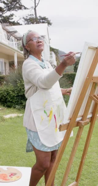 スローモーションでイーゼル上のシニアアフリカ系アメリカ人女性の絵画の垂直ビデオ 国内生活と高齢者のライフスタイル 変更なし — ストック動画